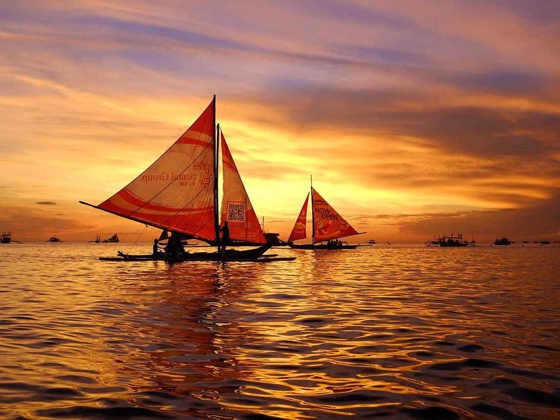 Barcos paraw com velas coloridas refletidos no mar dourado do p&ocirc;r do sol em Boracay