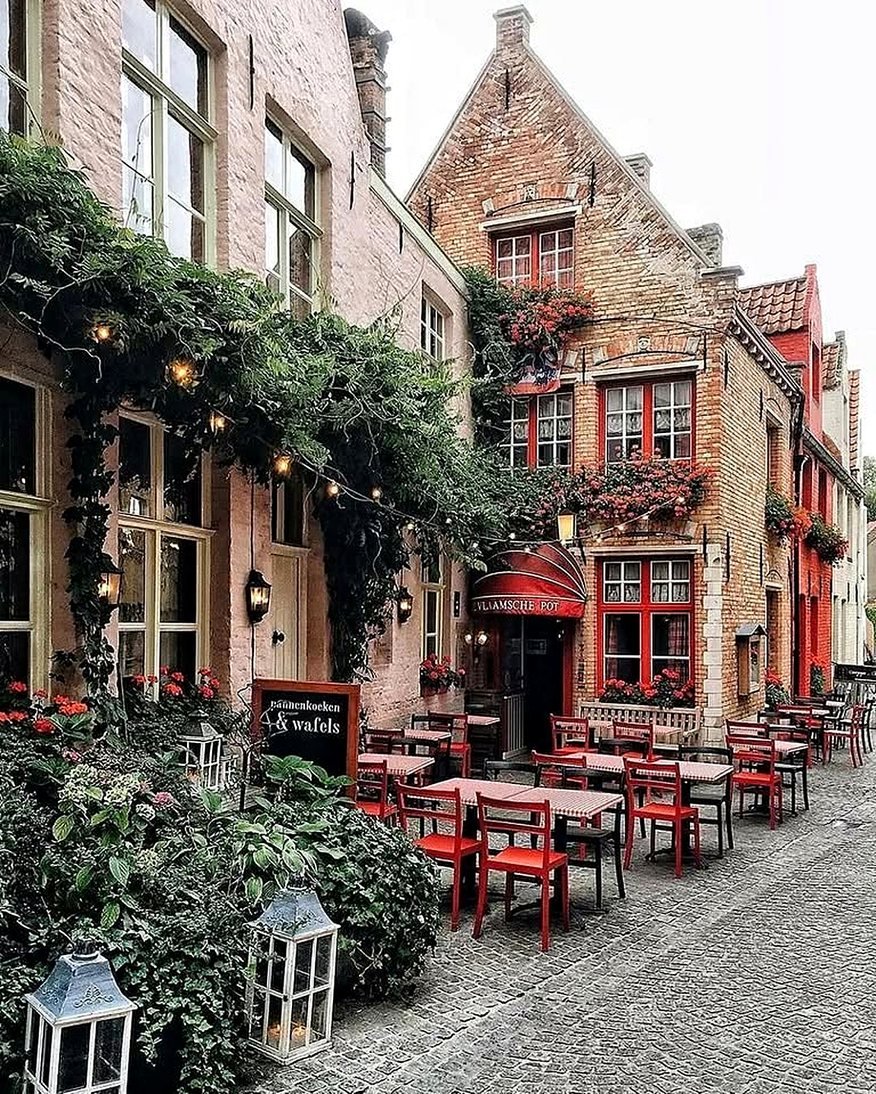 Restaurante com mesas vermelhas na calçada e fachada florida em uma rua de Bruges