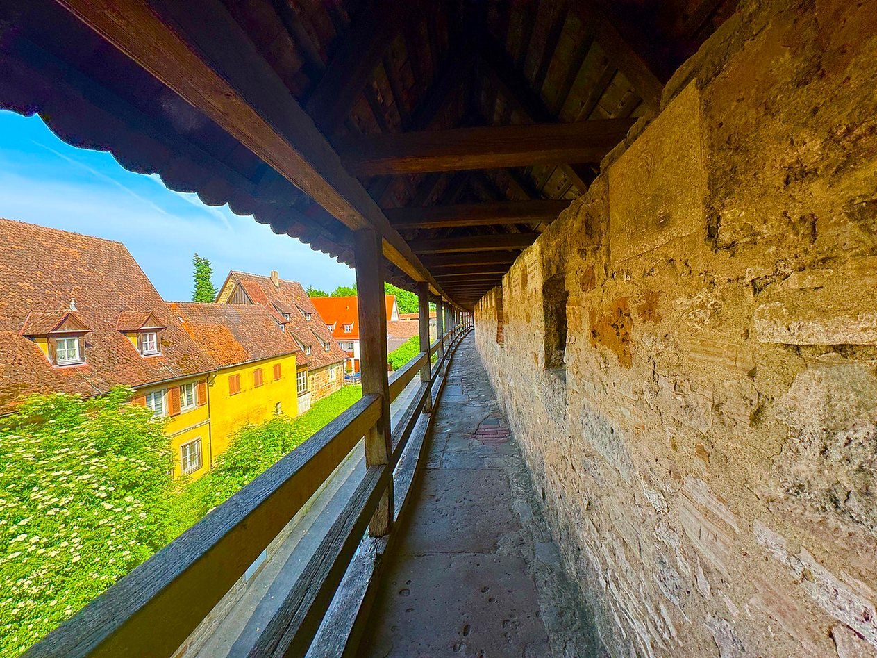 Caminho de pedra coberto sobre a muralha medieval de Rothenburg, ao lado de casas amarelas e telhados antigos