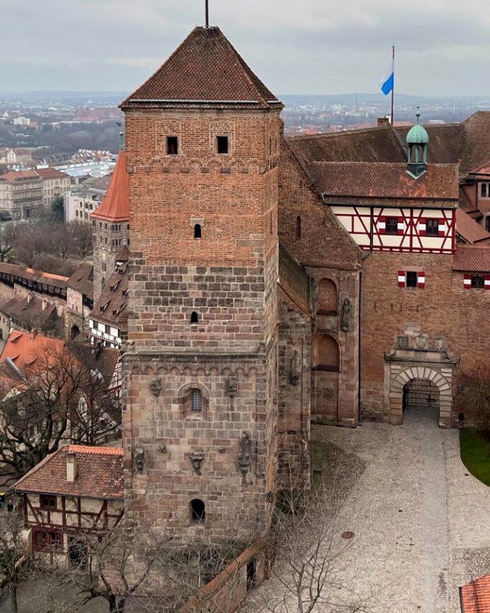 Pátio do Castelo Imperial Kaiserburg com torre de pedra e casas de enxaimel vermelhas e brancas, em Nuremberg