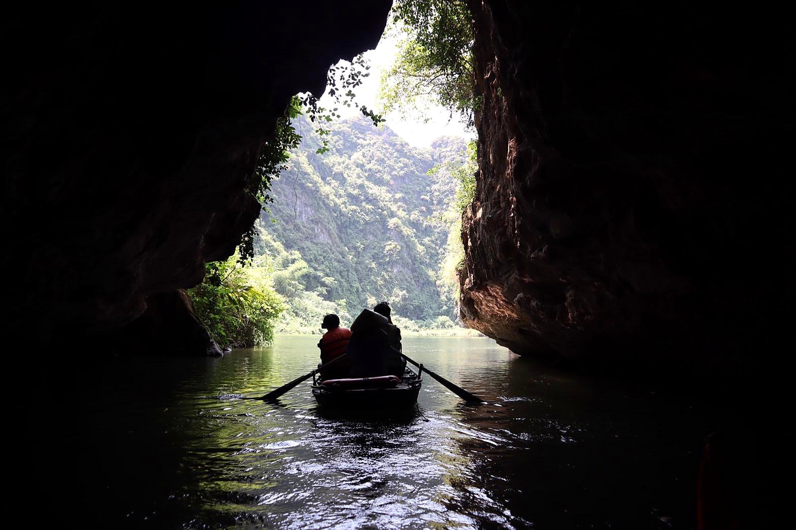 Barco a remo saindo de uma caverna em Trang An, Ninh Binh, com montanhas verdes ao fundo