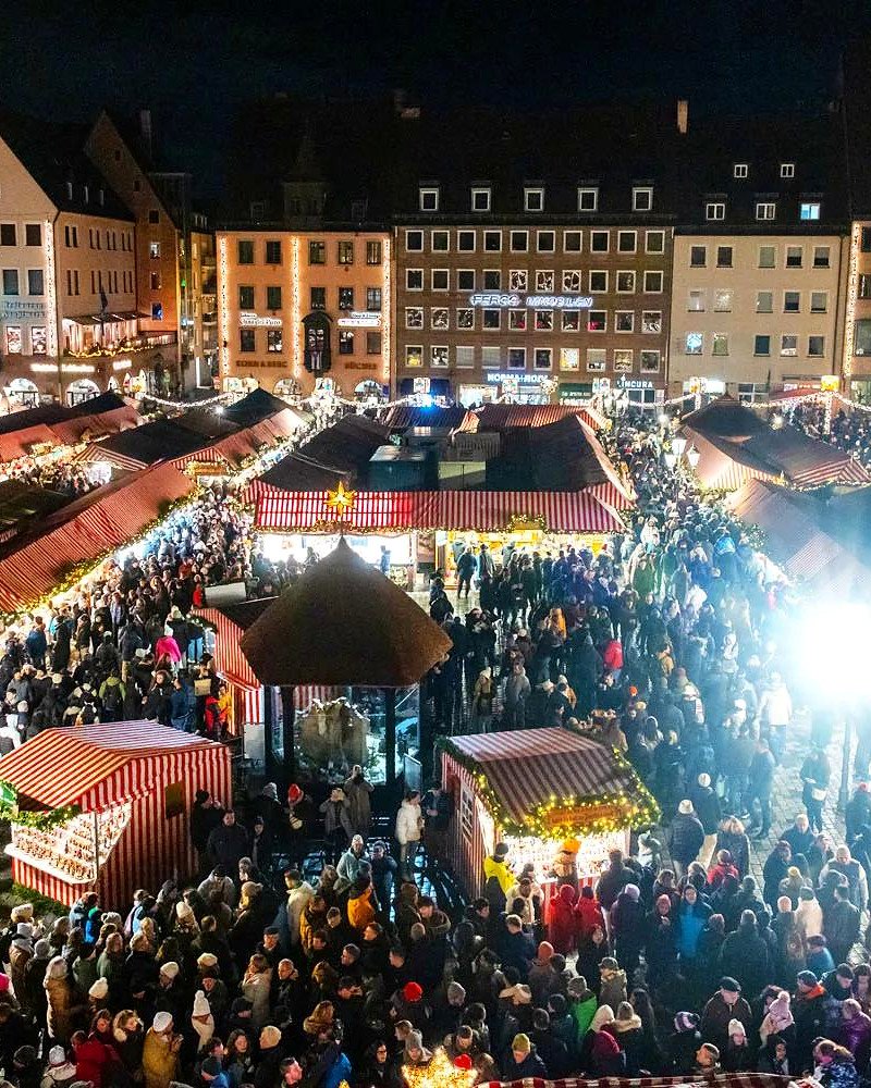 Vista do alto do mercado de Natal de Nuremberg lotado de visitantes entre barracas listradas de vermelho e branco