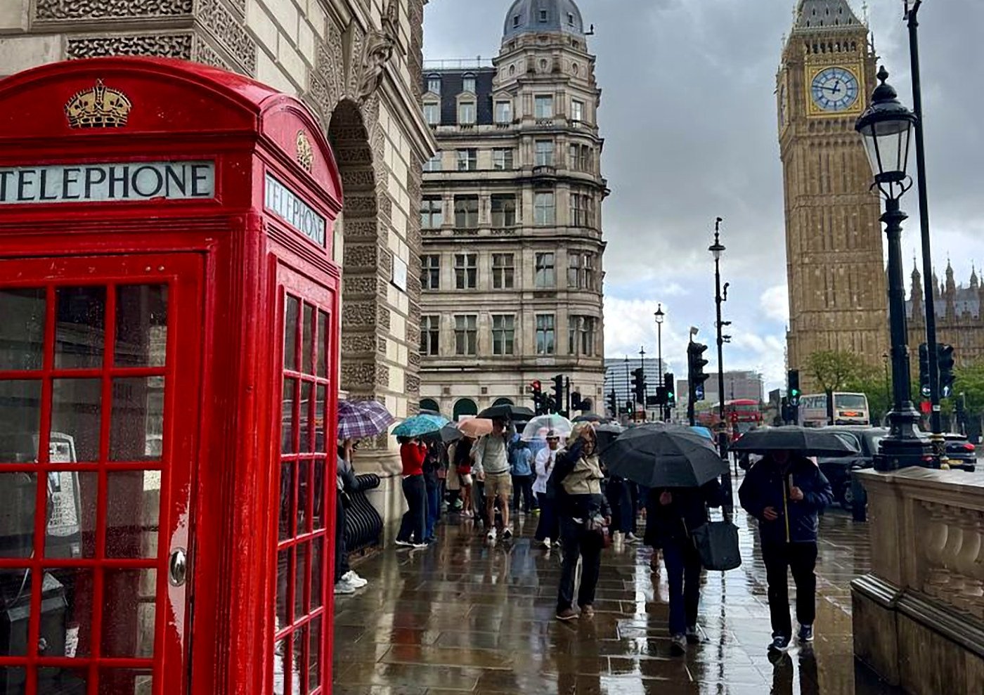Cabine telefônica vermelha e pessoas com guarda-chuvas em dia chuvoso perto do Big Ben