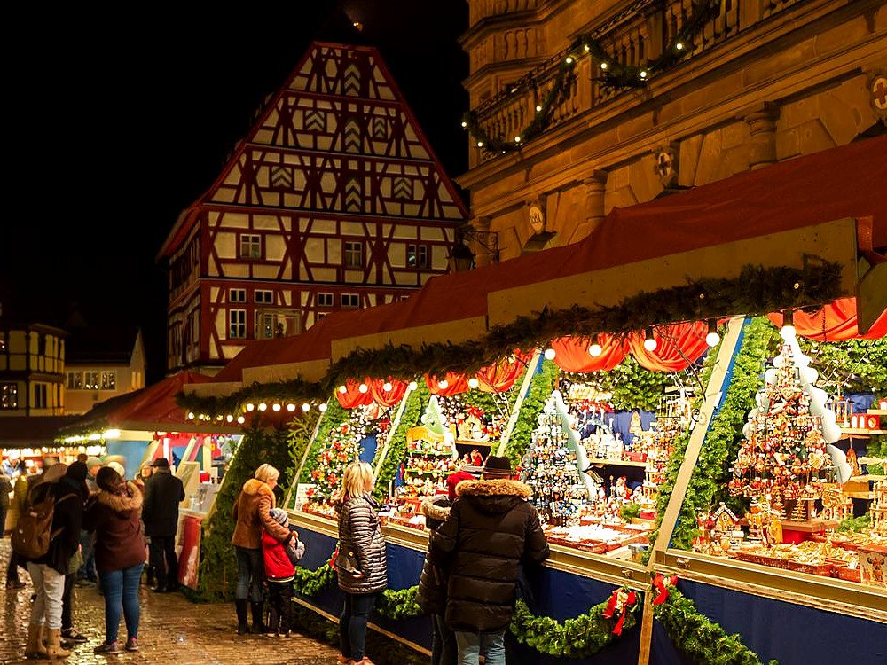 Barraca com enfeites de Natal artesanais no Reiterlesmarkt de Rothenburg, com casa de enxaimel iluminada ao fundo