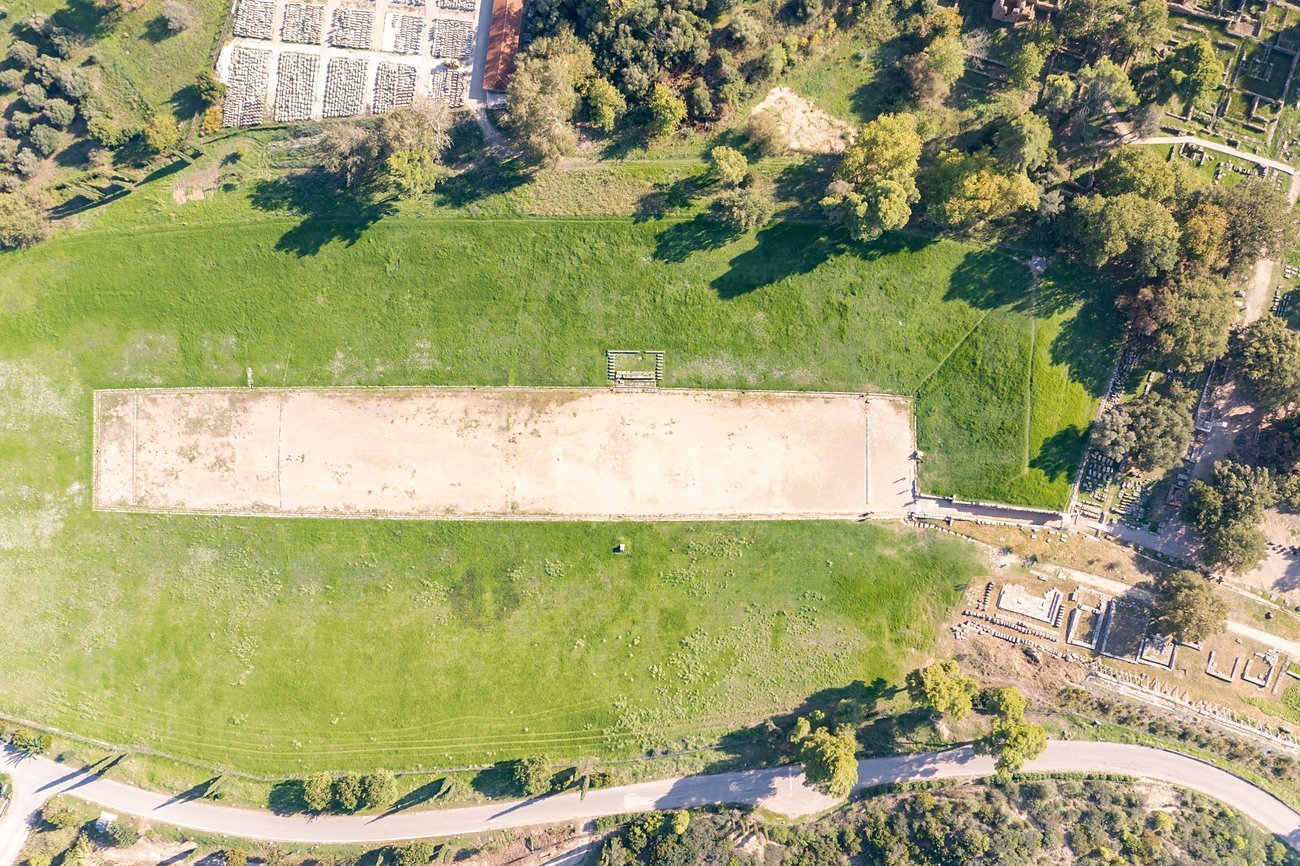 Vista a&eacute;rea da pista de terra do Est&aacute;dio Antigo de Ol&iacute;mpia cercada por encostas gramadas