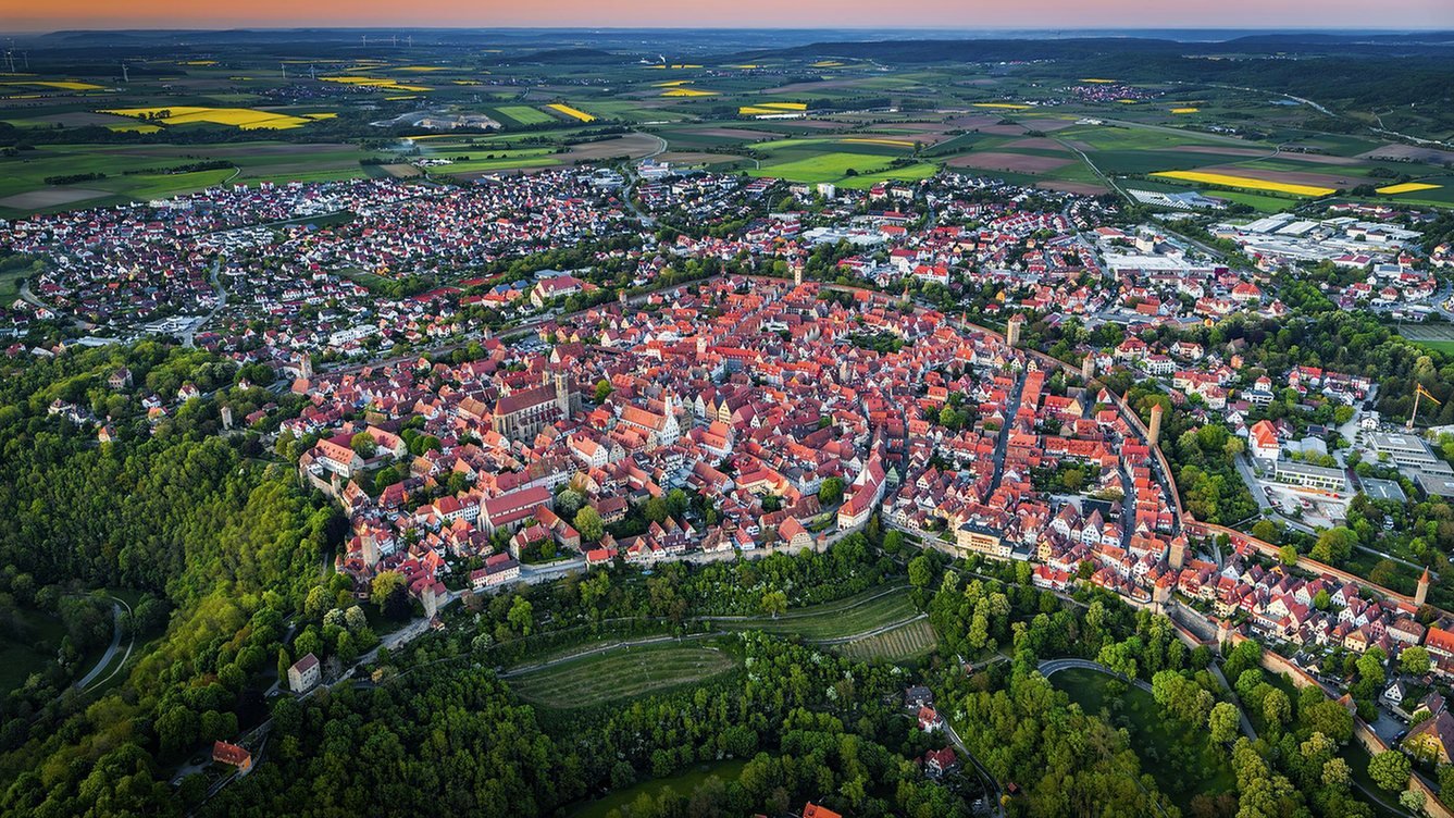Vista aérea da cidade medieval murada de Rothenburg ob der Tauber, na Alemanha, com telhados vermelhos, a Igreja de São Jacó e o vale do rio Tauber ao entardecer