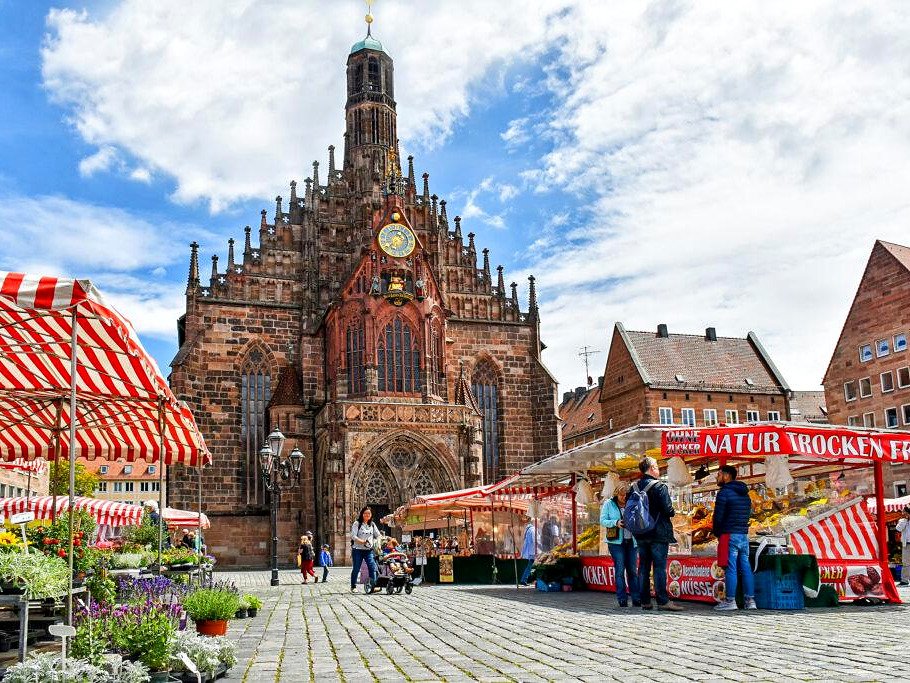 Fachada gótica da igreja Frauenkirche com relógio dourado e barracas da feira no Hauptmarkt de Nuremberg