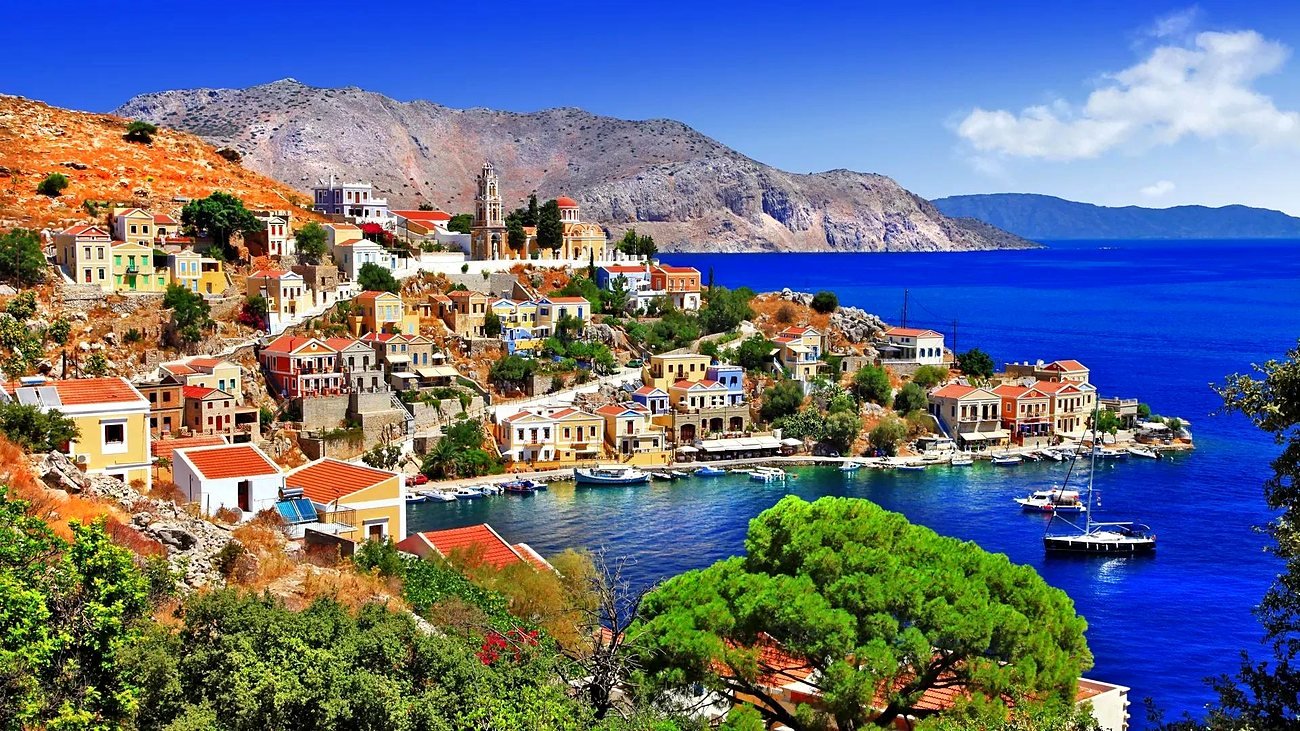 Vista do porto de Symi com casas coloridas na encosta e mar azul