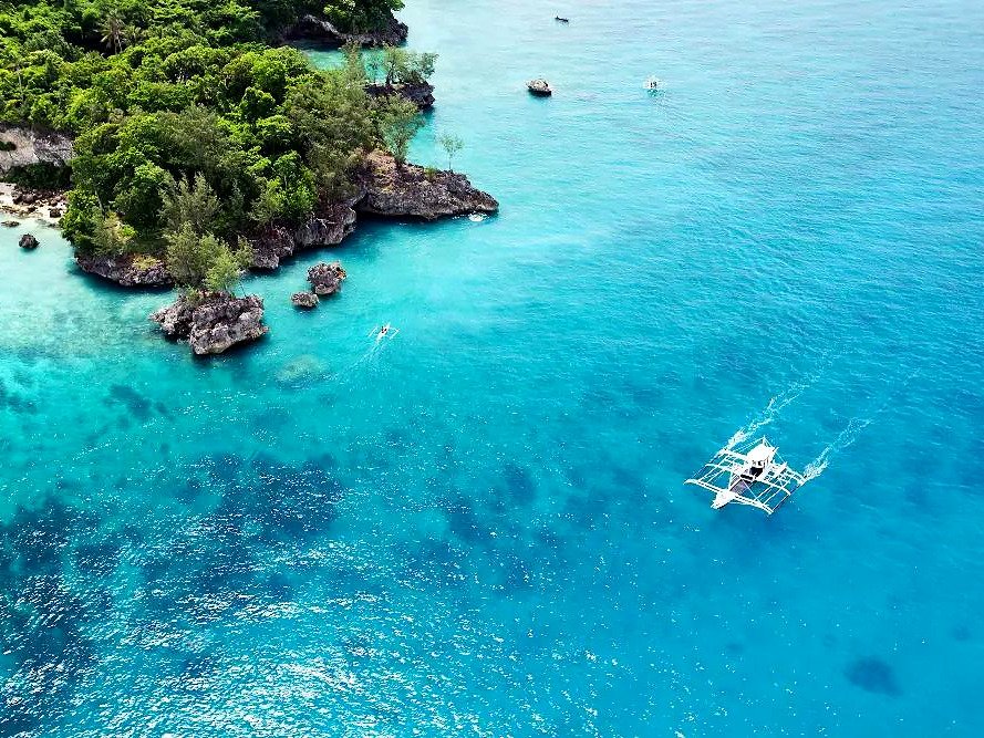 Barco bangka navegando no mar azul ao lado de enseada rochosa em passeio de island hopping em Boracay