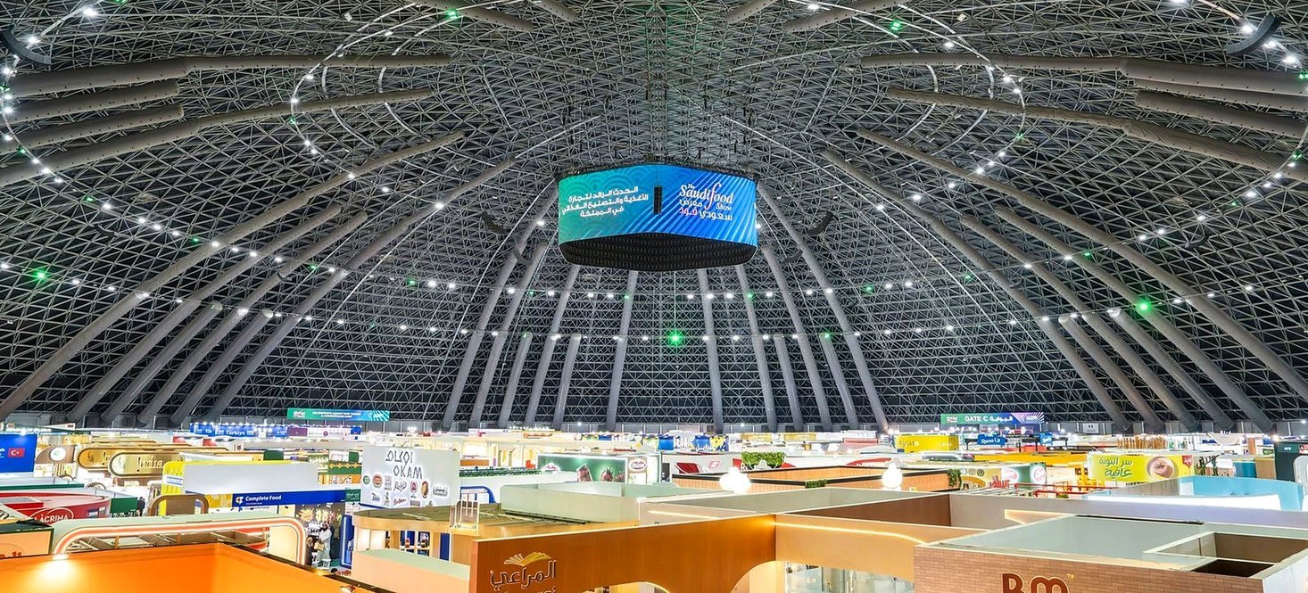 Interior do Jeddah Superdome durante feira de alimentos, com a enorme cúpula metálica