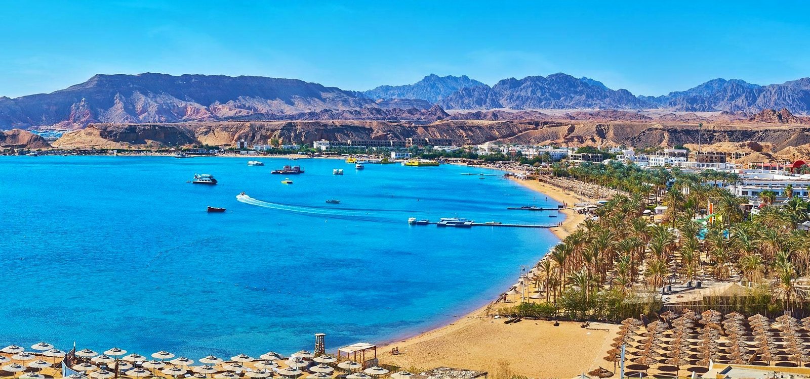 Baía de Sharm el-Sheikh com mar azul, praia, palmeiras e as montanhas do Sinai ao fundo