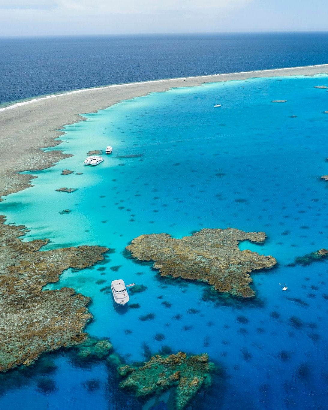 Recifes de coral e lagoa azul-turquesa do Mar Vermelho vistos do alto, com barcos de mergulho