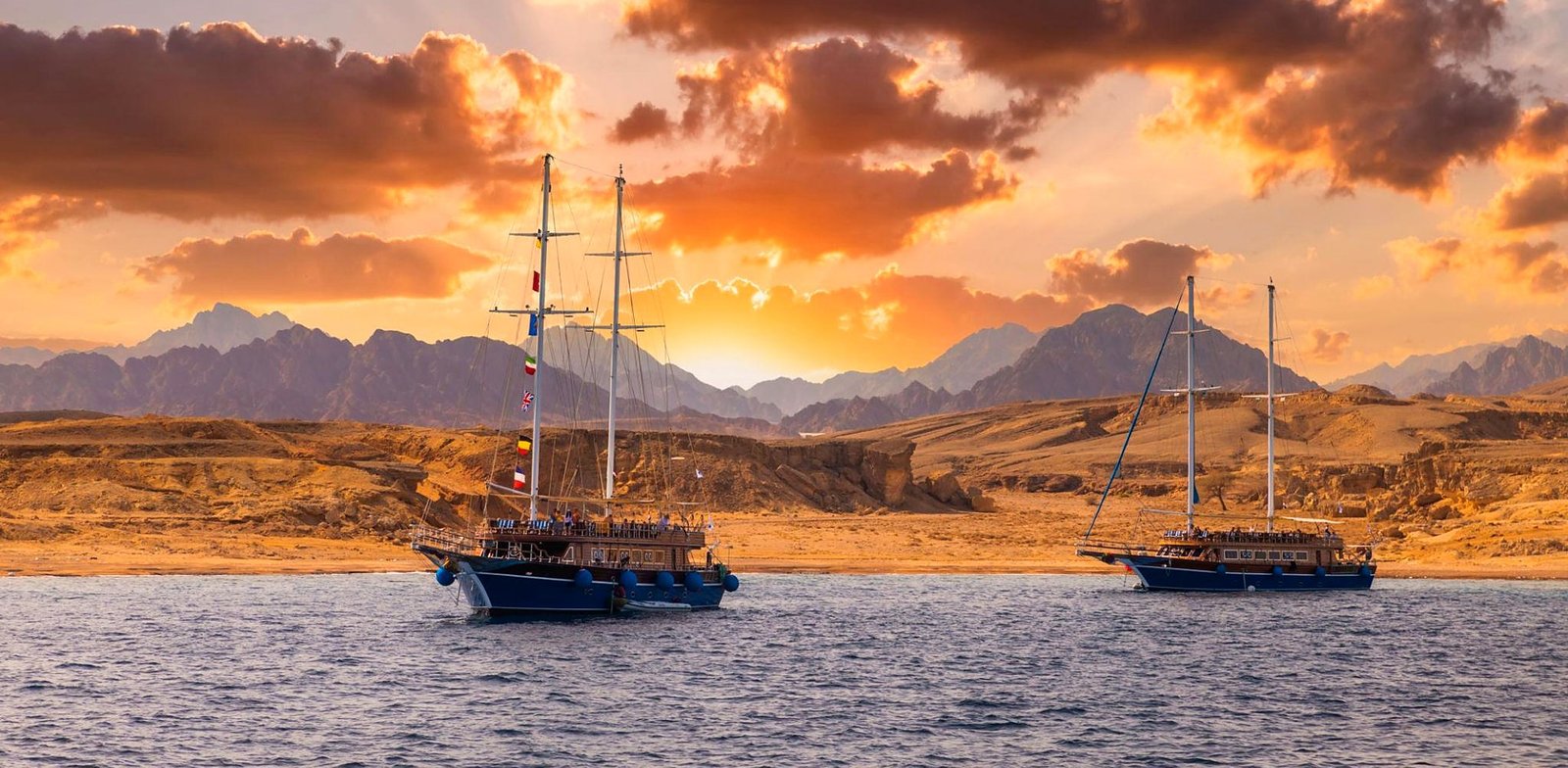 Veleiros de passeio no Mar Vermelho ao pôr do sol, com o deserto e as montanhas do Sinai ao fundo