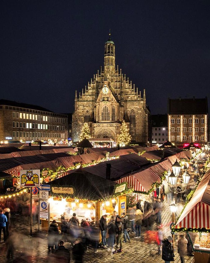 Barracas listradas e iluminadas do Christkindlesmarkt diante da Frauenkirche, em Nuremberg, à noite