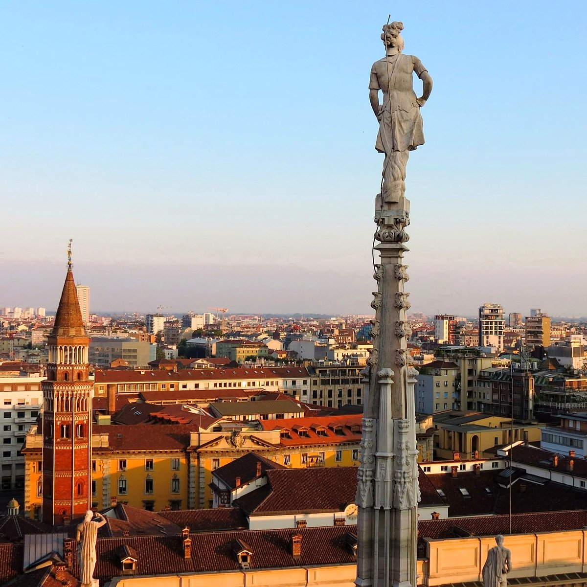 Vista dos terraços do Duomo de Milão com estátua no pináculo e telhados da cidade