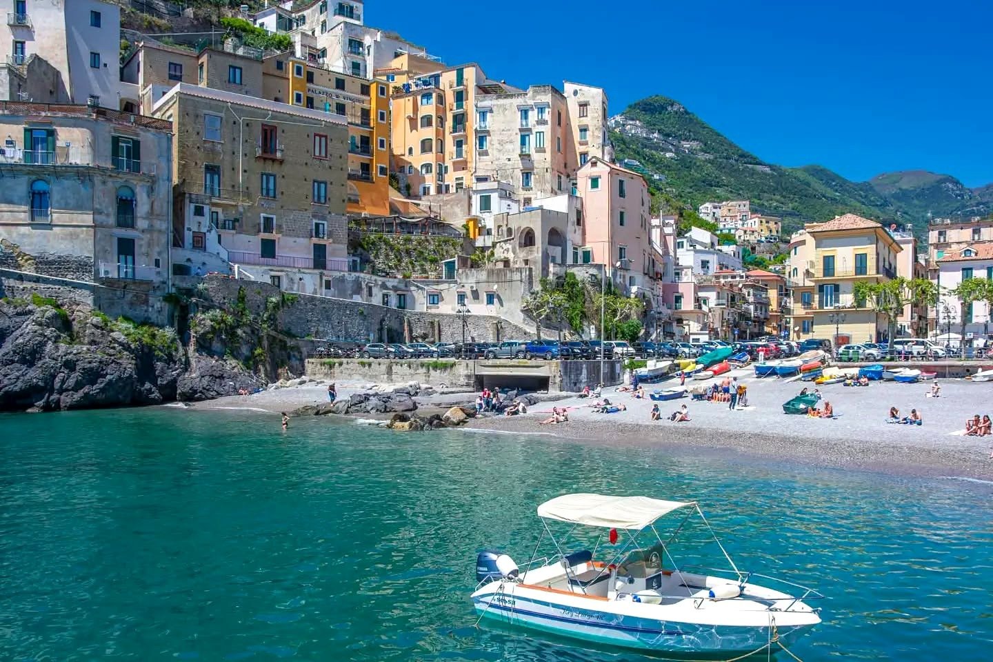 Praia de Minori com barco ancorado e casas coloridas