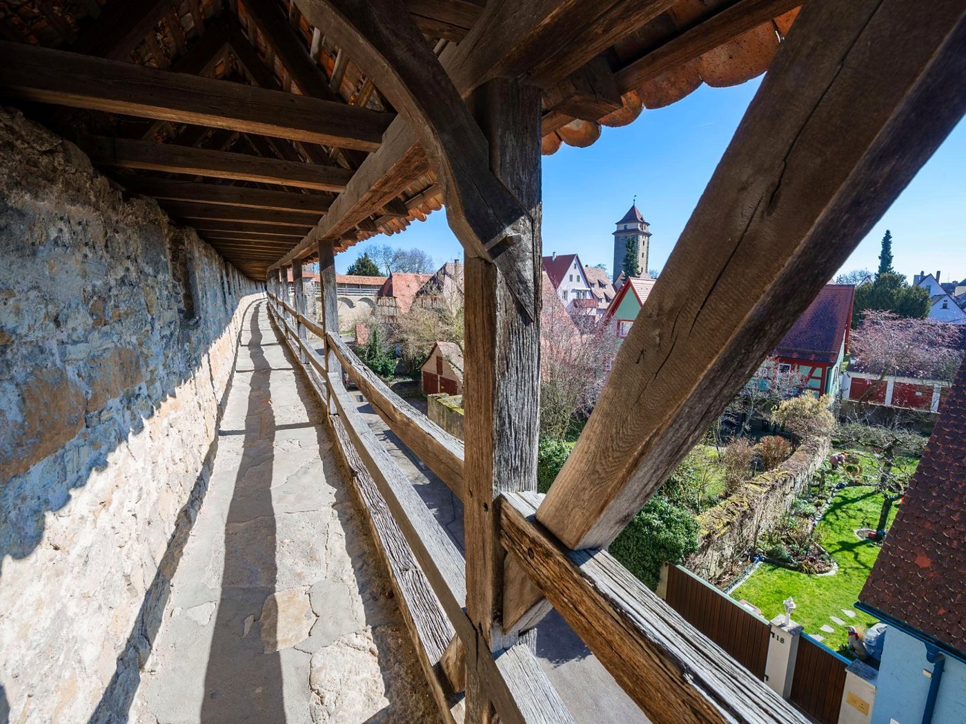Passarela coberta de madeira sobre a muralha de Rothenburg, com vista para casas, jardins e uma torre medieval