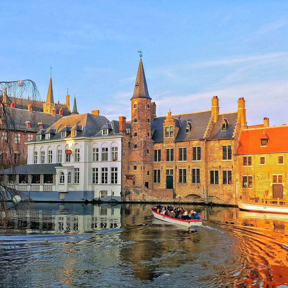 Rozenhoedkaai em Bruges iluminado pelo sol da tarde, com barco turístico no canal