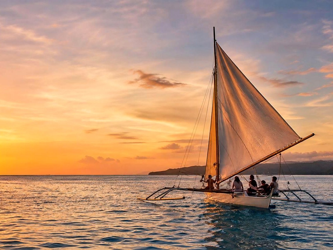Turistas em passeio de barco paraw com vela branca no p&ocirc;r do sol de Boracay