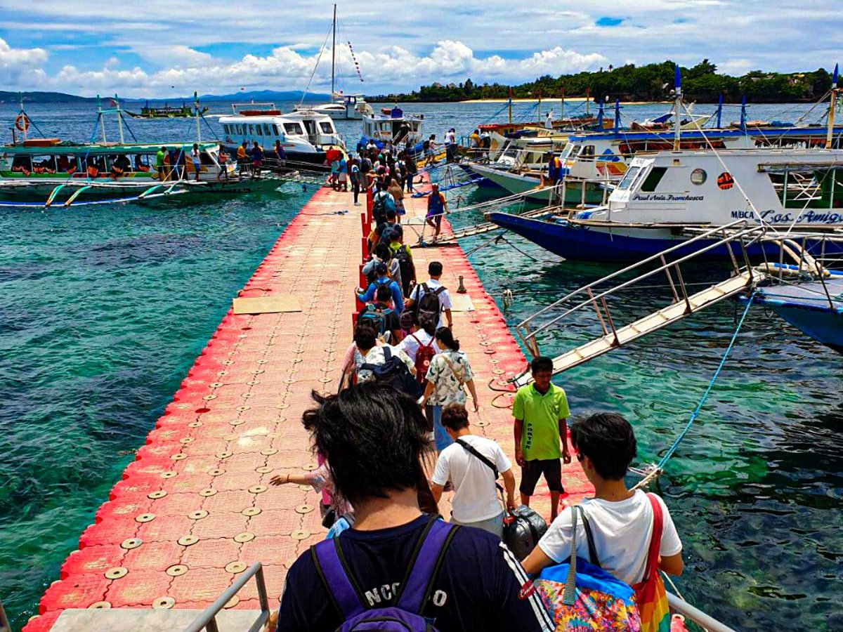 Turistas com malas caminhando pelo p&iacute;er flutuante de chegada a Boracay, entre barcos de passageiros