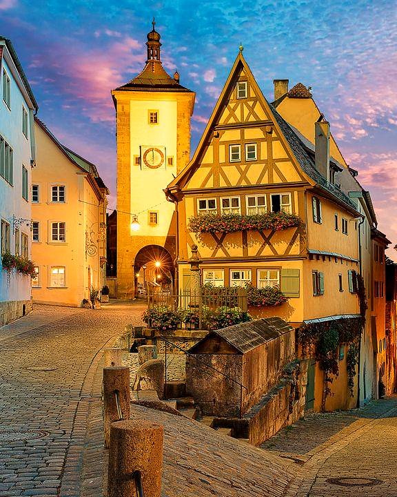 Plönlein ao pôr do sol, com céu rosado, casa amarela e torres medievais de Rothenburg ob der Tauber