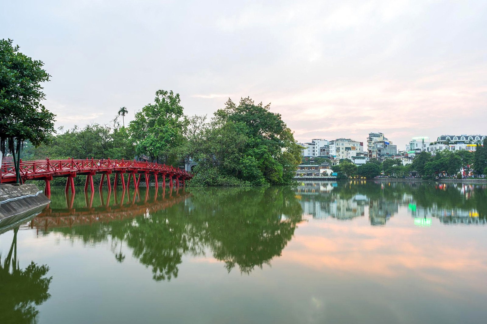 Ponte vermelha The Huc refletida no Lago Hoan Kiem, em Han&oacute;i, ao entardecer