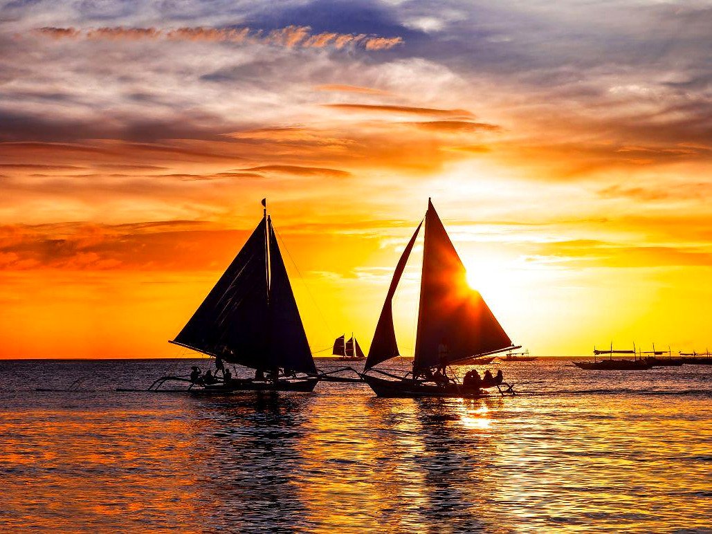 Silhueta de dois barcos paraw navegando no p&ocirc;r do sol laranja em Boracay