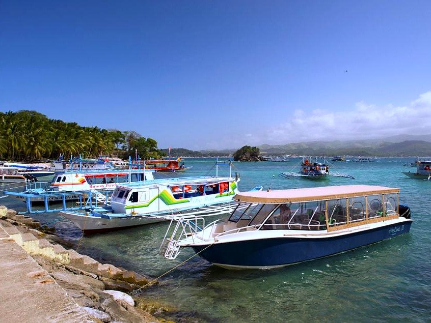 Barcos de passageiros atracados no porto de Boracay, com mar azul e coqueiros