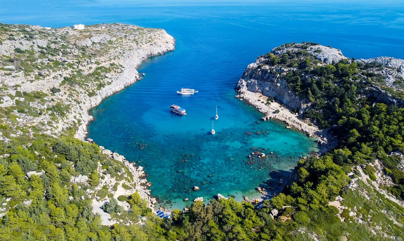 Vista aérea da enseada de Anthony Quinn Bay, em Rodes, com água azul-turquesa entre rochas e pinheiros