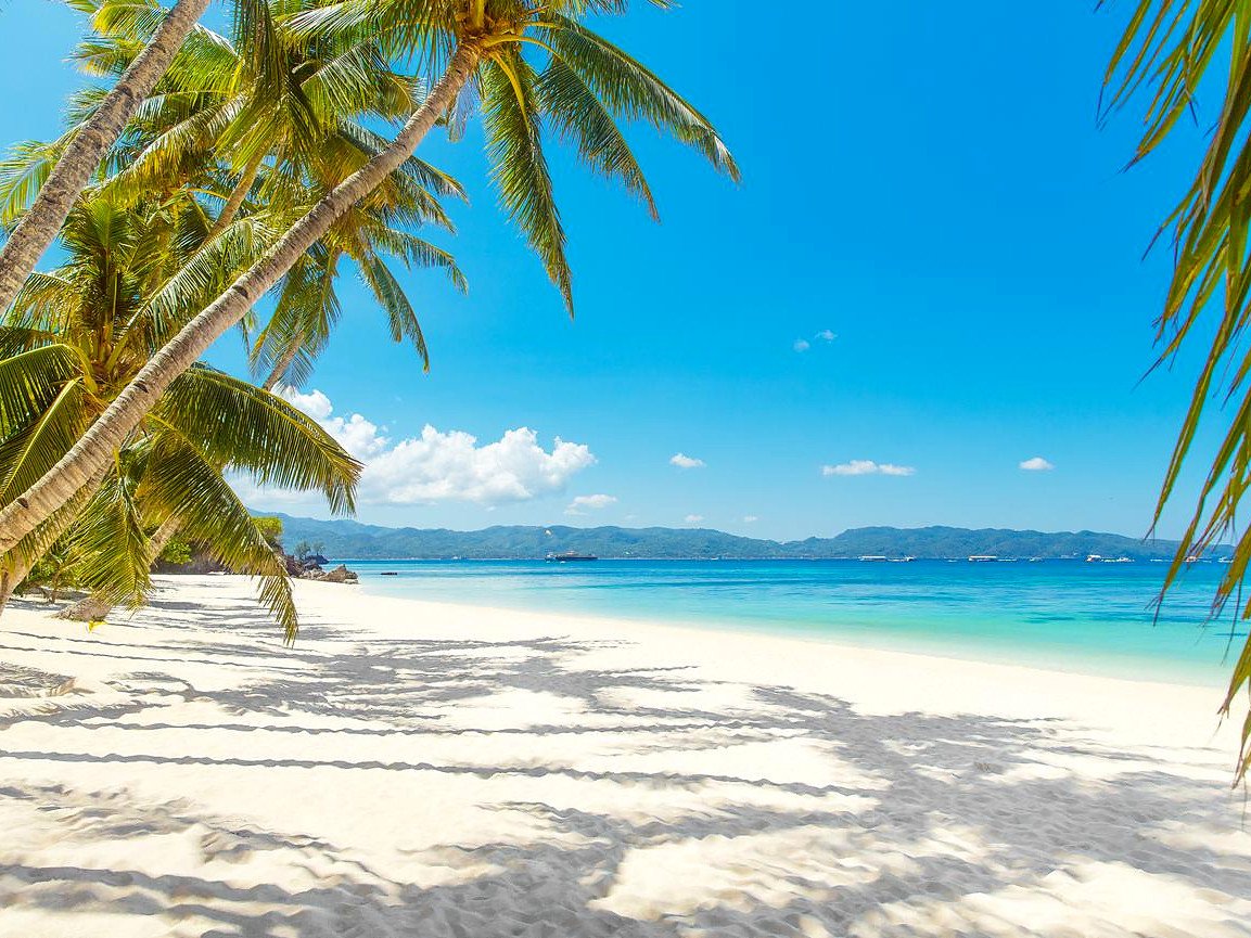 Coqueiros fazendo sombra na areia branca de praia em Boracay, com mar azul e montanhas ao fundo
