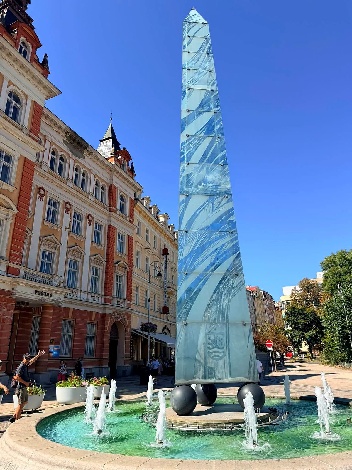 Fonte com obelisco de vidro diante do prédio dos Correios em Karlovy Vary