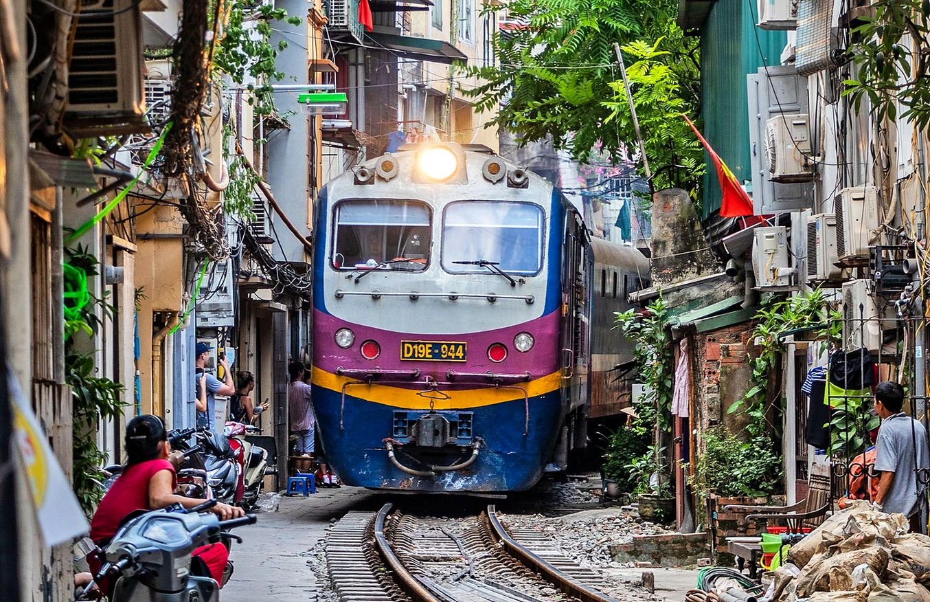 Trem passando entre casas estreitas na Rua do Trem (Train Street), em Han&oacute;i, com moradores observando