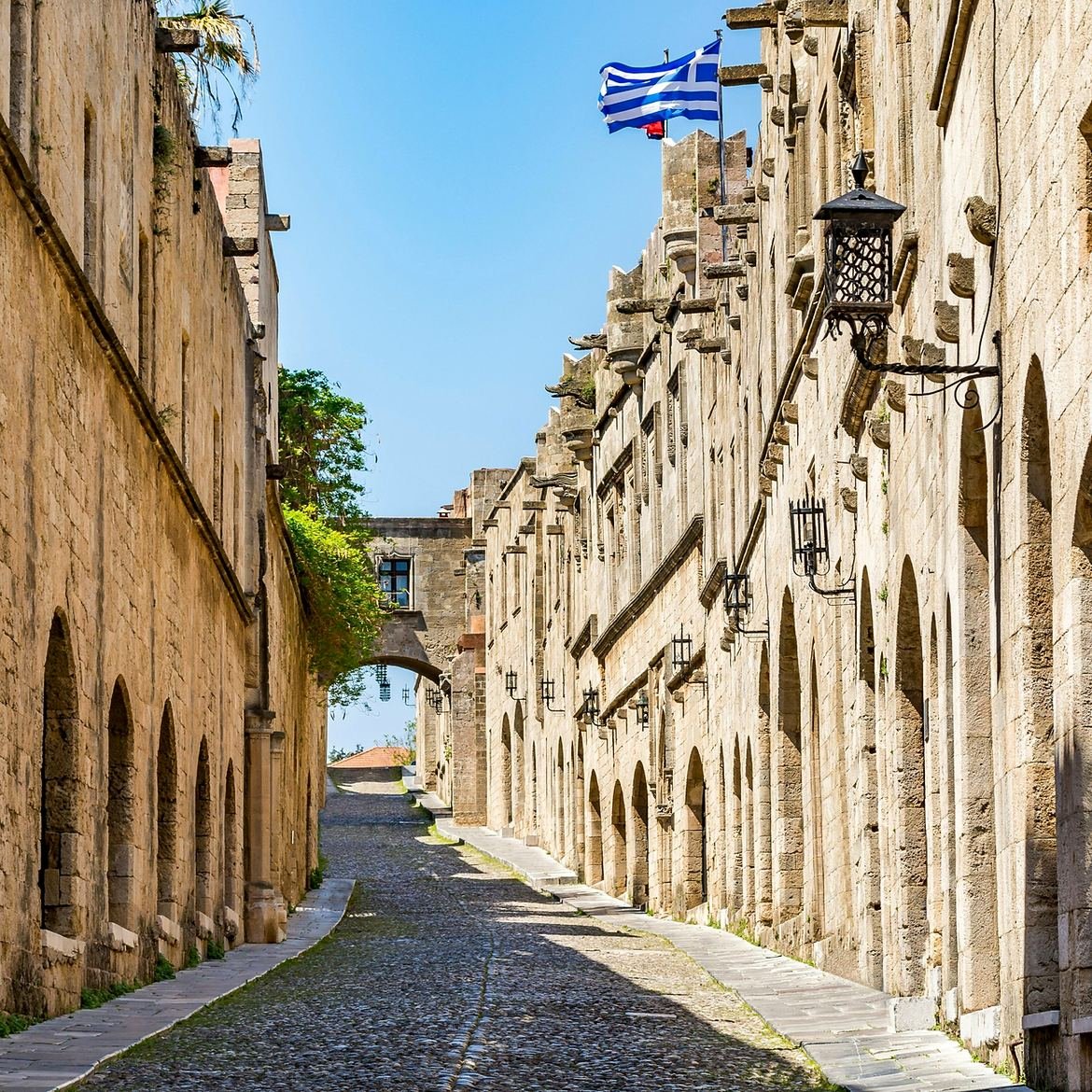Rua dos Cavaleiros, rua de pedra com fachadas medievais e a bandeira da Grécia na Cidade Medieval de Rodes
