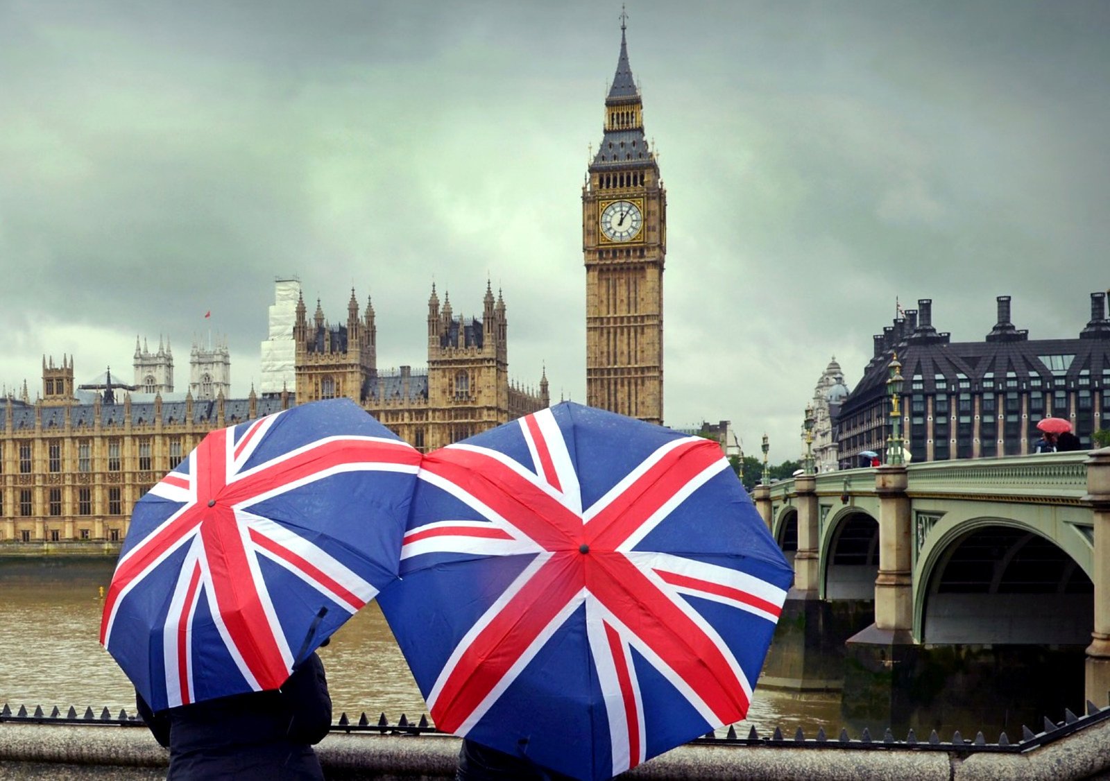 Turistas com guarda-chuvas da bandeira britânica olhando o Big Ben em um dia nublado em Londres