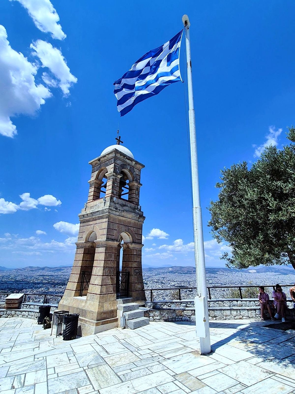 Bandeira da Grécia e campanário no alto do Monte Licabeto, com vista de Atenas