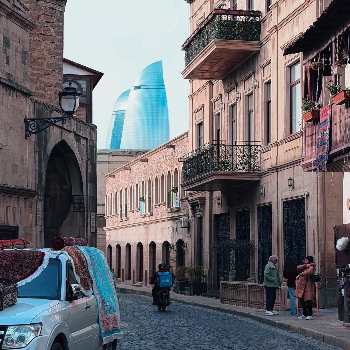 Rua da Cidade Velha de Baku com tapetes à venda e as Flame Towers ao fundo