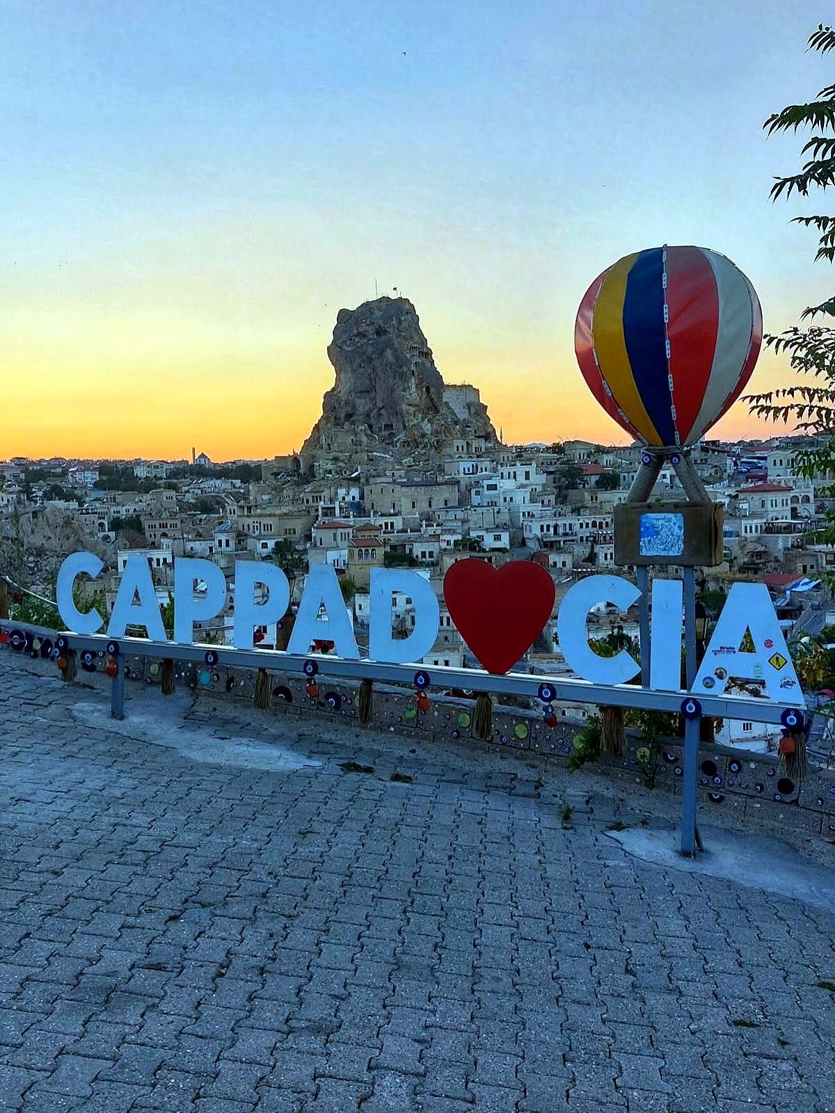 Letreiro Cappadocia com castelo de rocha e vilarejo ao pôr do sol