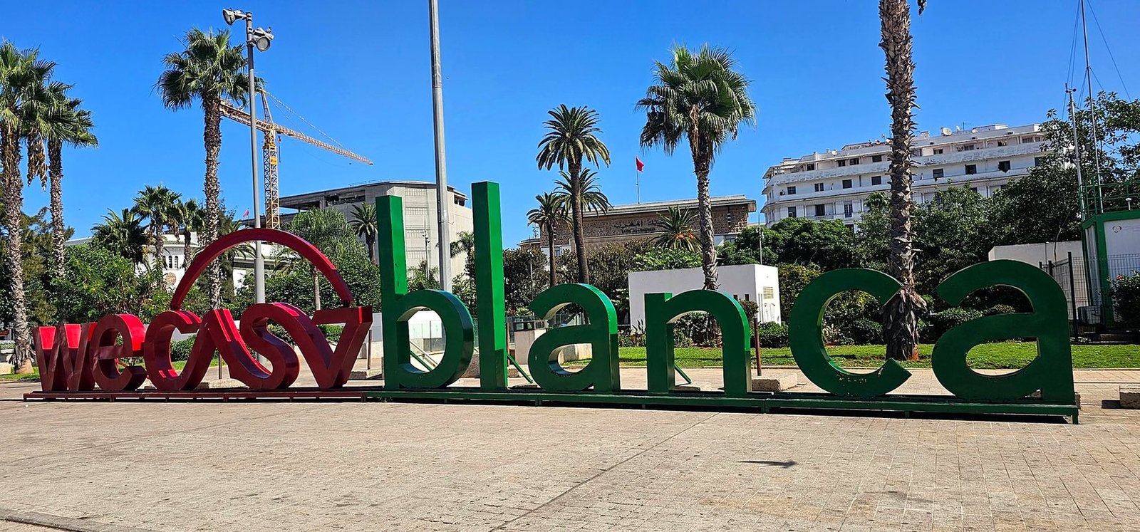 Letreiro gigante WeCasablanca em vermelho e verde entre palmeiras no centro da cidade