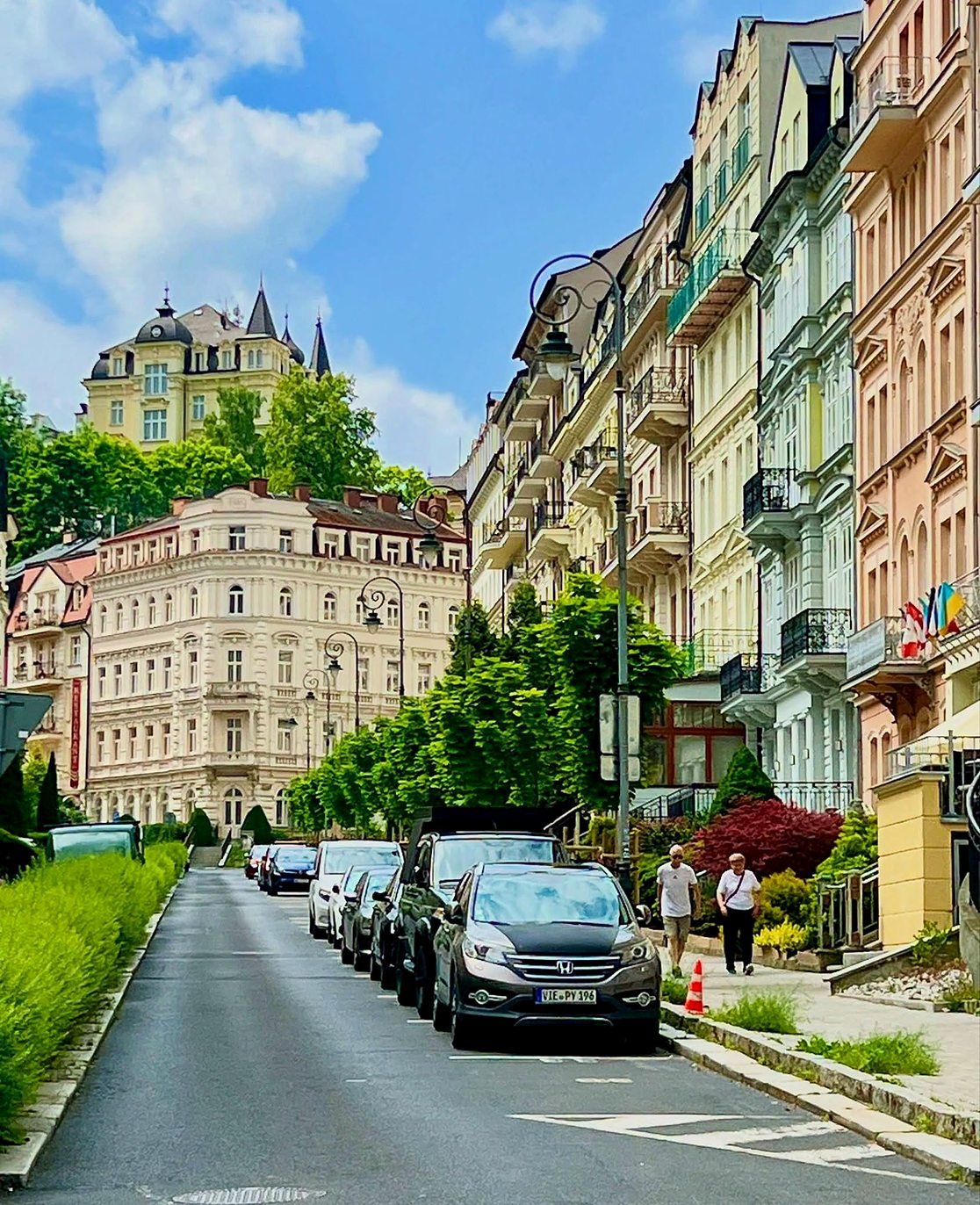 Rua arborizada com prédios da Belle Époque subindo a colina em Karlovy Vary