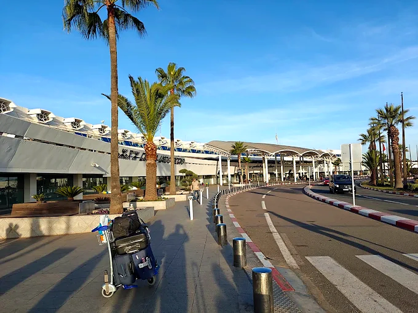 Área de desembarque do Aeroporto Internacional Mohammed V de Casablanca com palmeiras e carrinho de malas