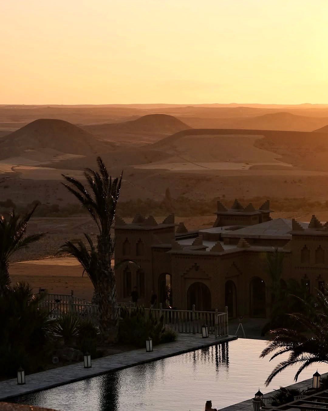 Pôr do sol sobre as colinas do Deserto de Agafay com hotel de estilo kasbah e piscina