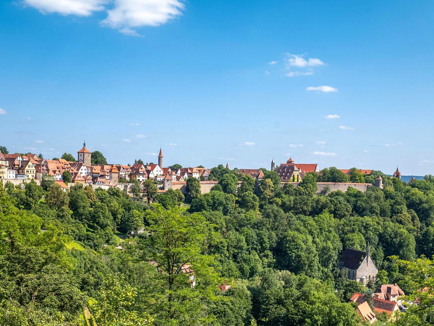 Cidade murada de Rothenburg no alto do morro, acima da mata verde do vale do rio Tauber