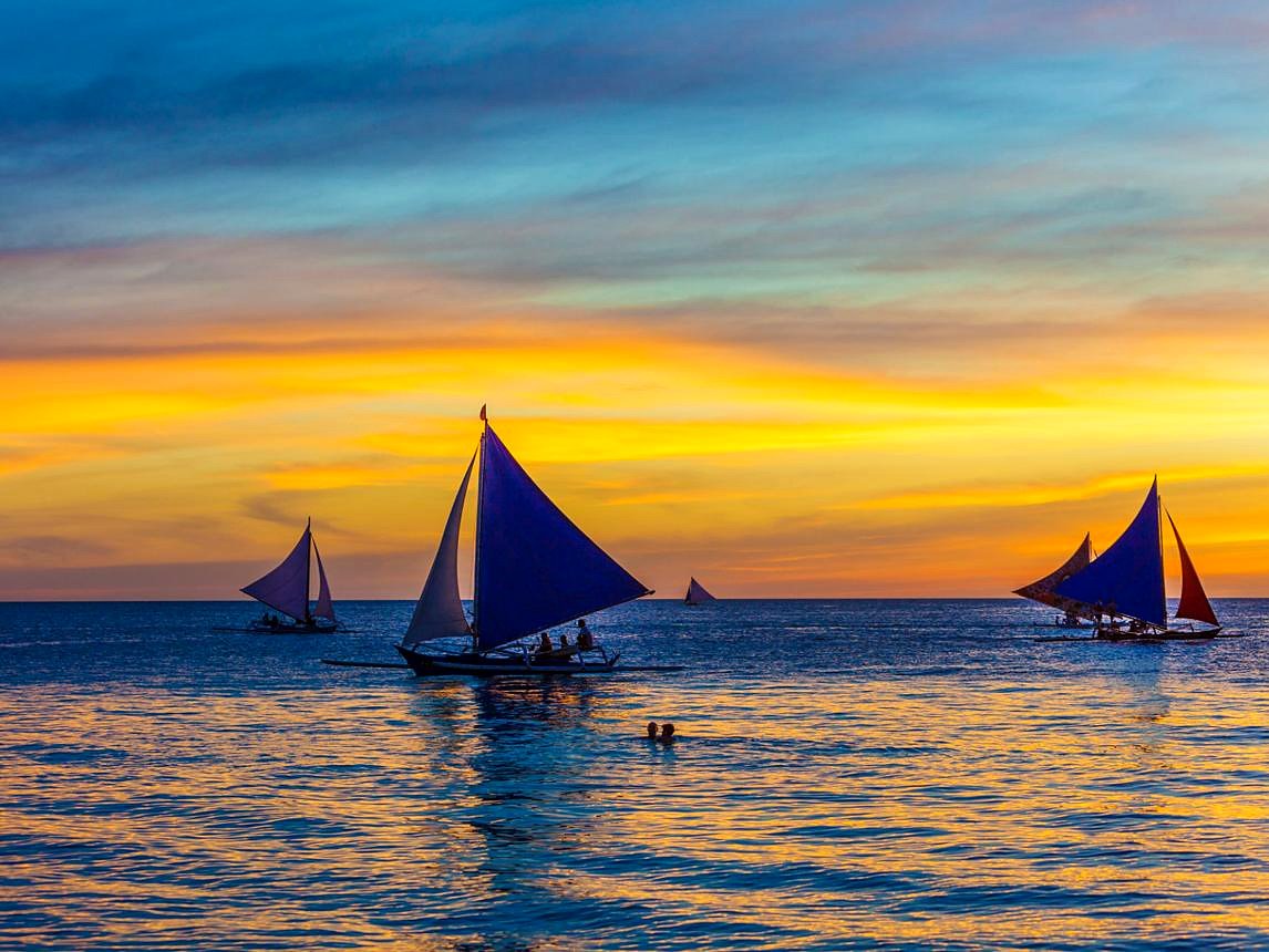 Veleiros paraw com velas azuis e vermelhas no crep&uacute;sculo em frente &agrave; White Beach de Boracay