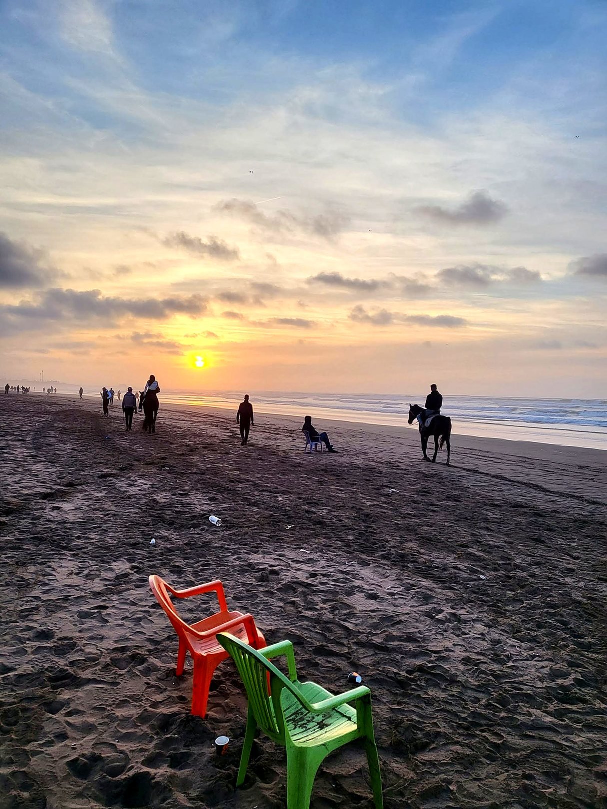 Pôr do sol na praia de Aïn Diab em Casablanca, com pessoas caminhando e cavalgando na areia