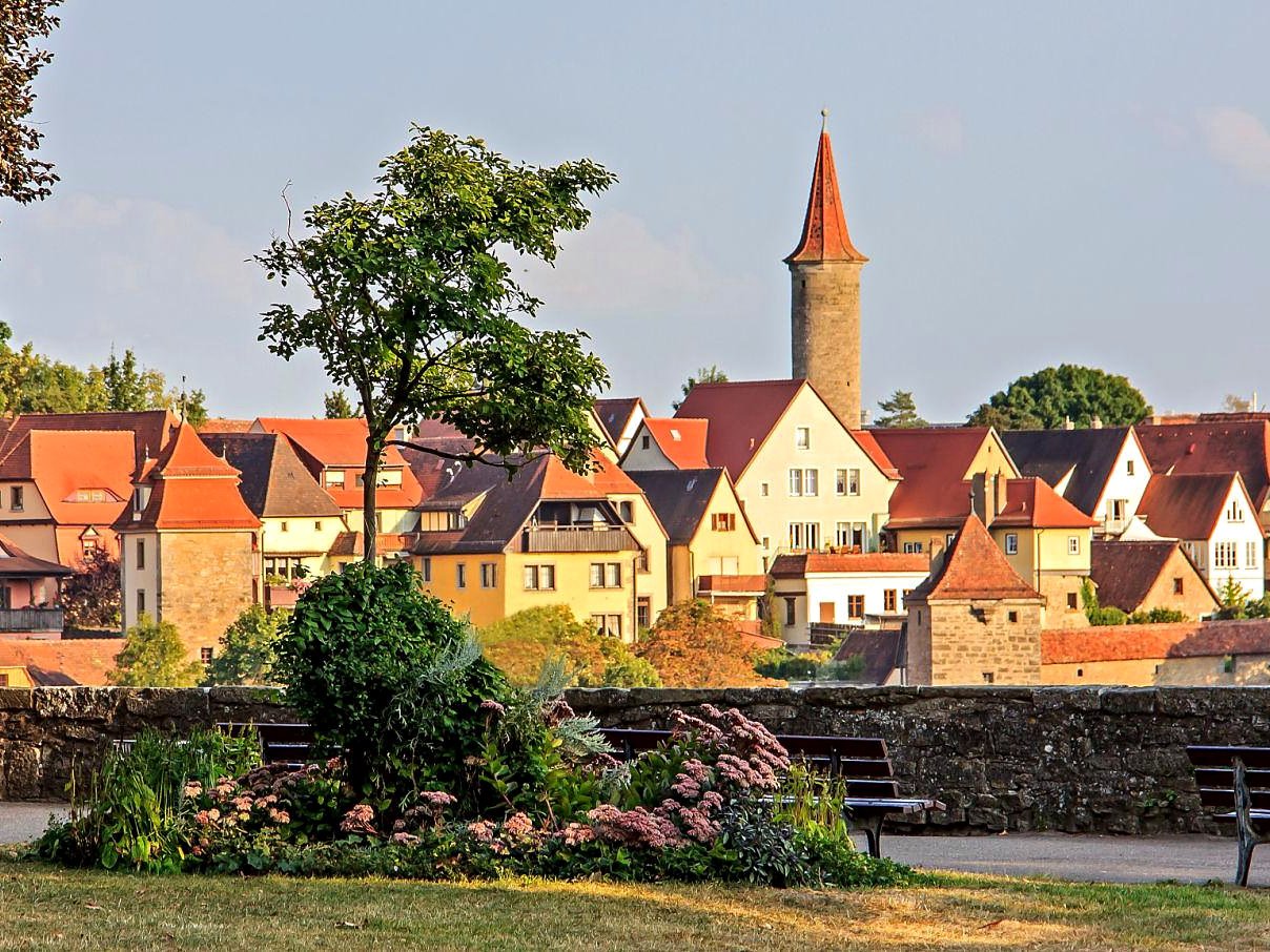 Vista do Burggarten com bancos e flores diante das casas e torres de Rothenburg ob der Tauber ao entardecer